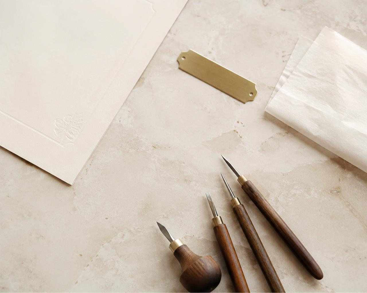 Engraving tools, ivory paper and a brass nameplate on pale stone